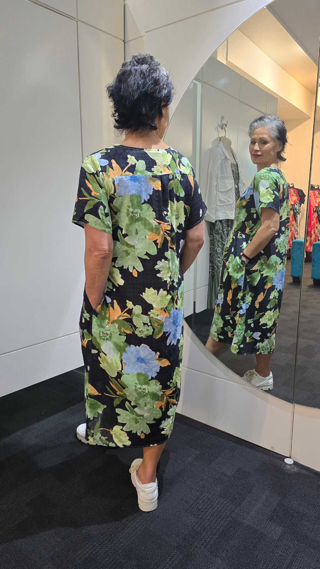 Woman wearing a floral dress standing in front of a mirror. Pleat Front Dress Black