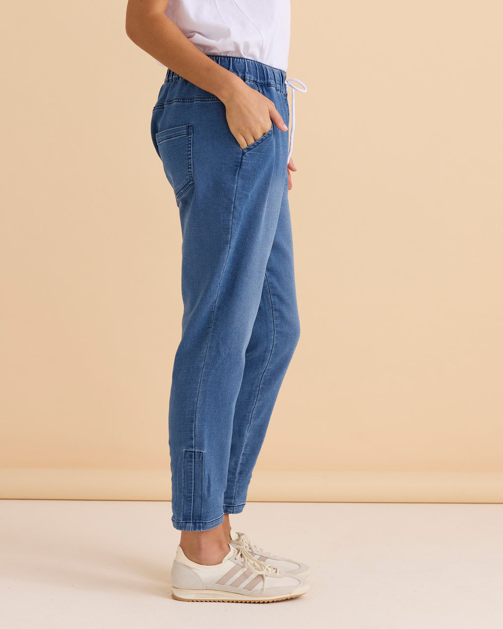 Person wearing blue jogger pants with a white top against a beige background