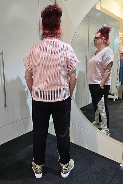 Person wearing a light pink knit top with floral patterns and black pants, standing against a white wall.
Italian Metallic Stars Top Pink