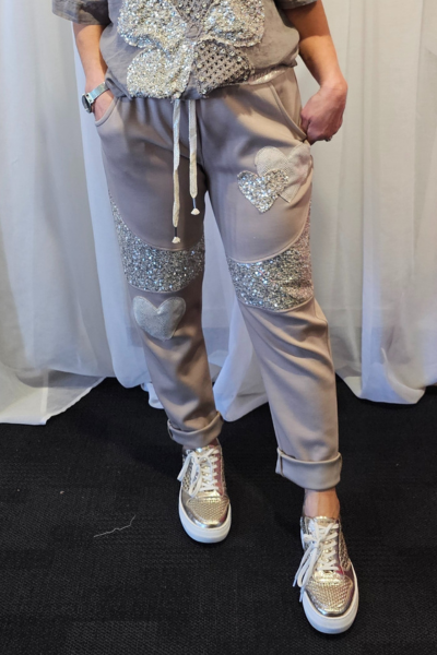 Person wearing a gray outfit with embellishments in front of white curtains
Italian Relax Heart Pants Taupe