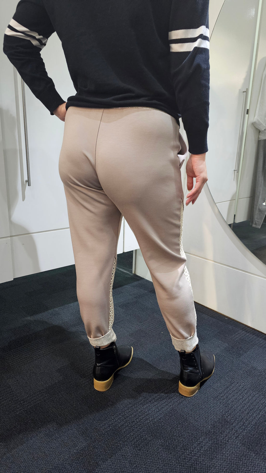 Person wearing a navy sweater with white star design and beige pants with mesh panels in a bathroom.
