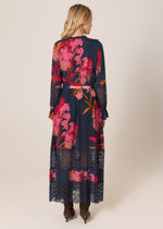 Woman wearing a long floral dress with a lace overlay on a beige background