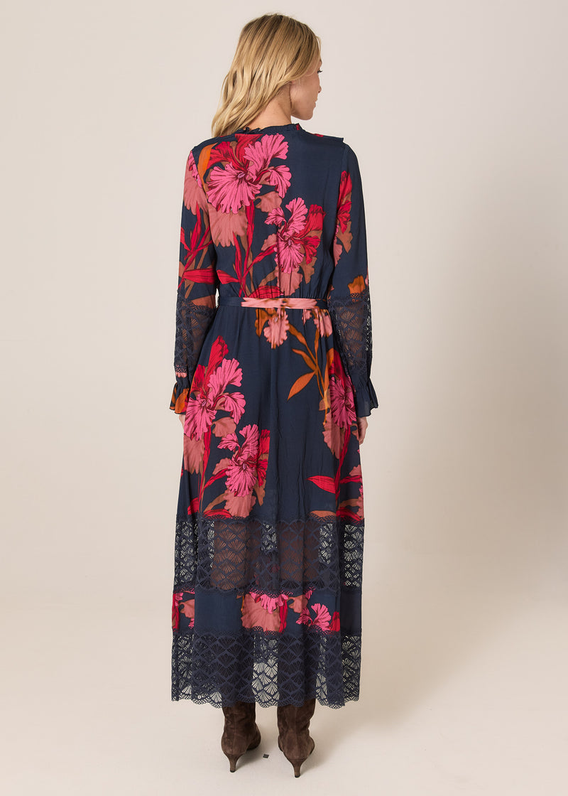 Woman wearing a long floral dress with a lace overlay on a beige background
