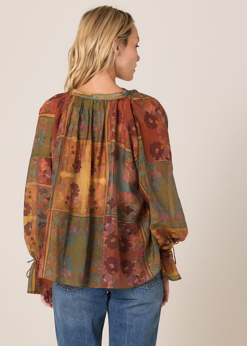 Woman wearing a patterned blouse with long sleeves and blue jeans on a beige background
Bohemian Top Nouveau Floral Green