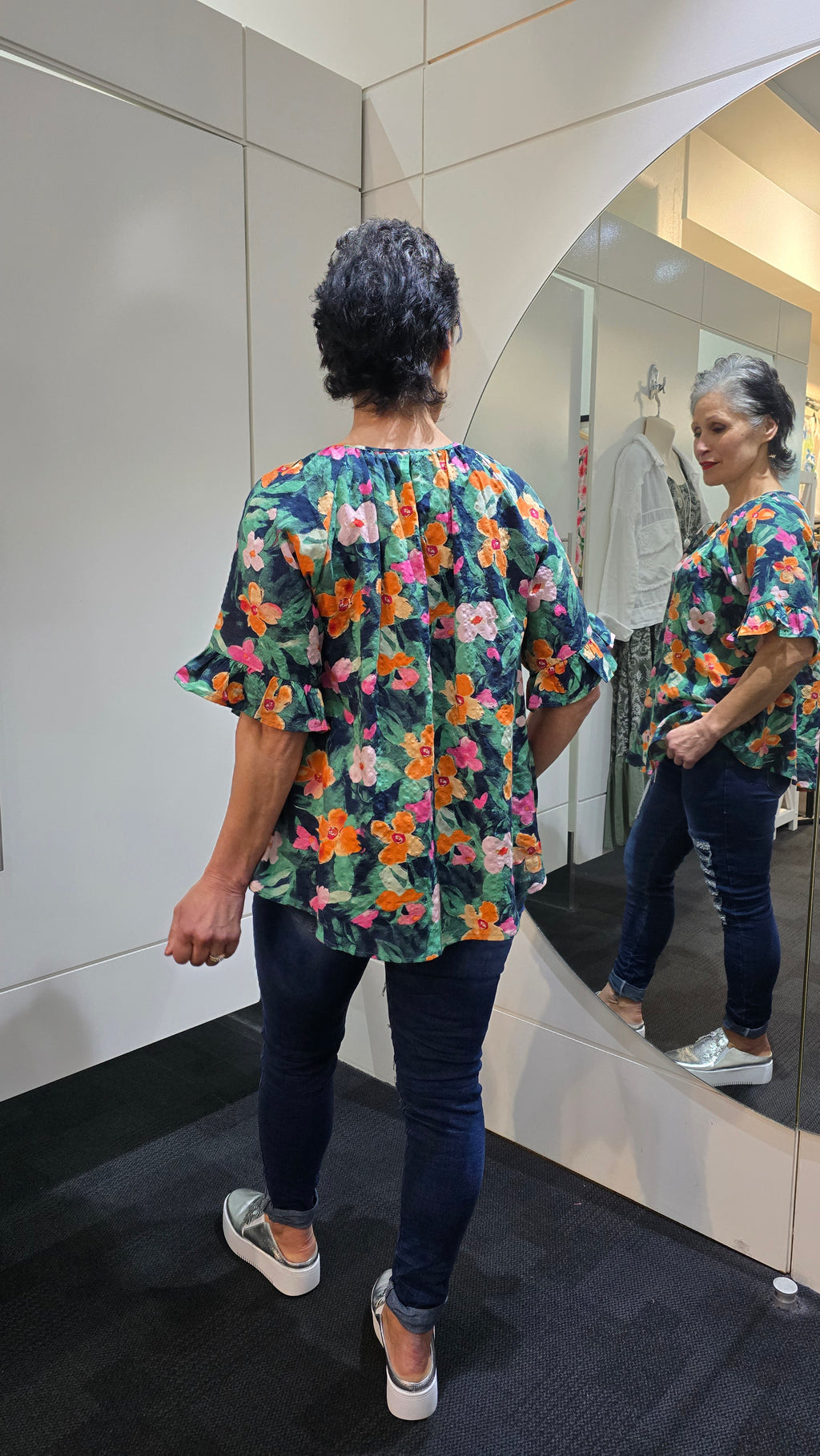 Person wearing a colorful floral shirt and dark jeans standing in a store. Tie Neck Top Navy
