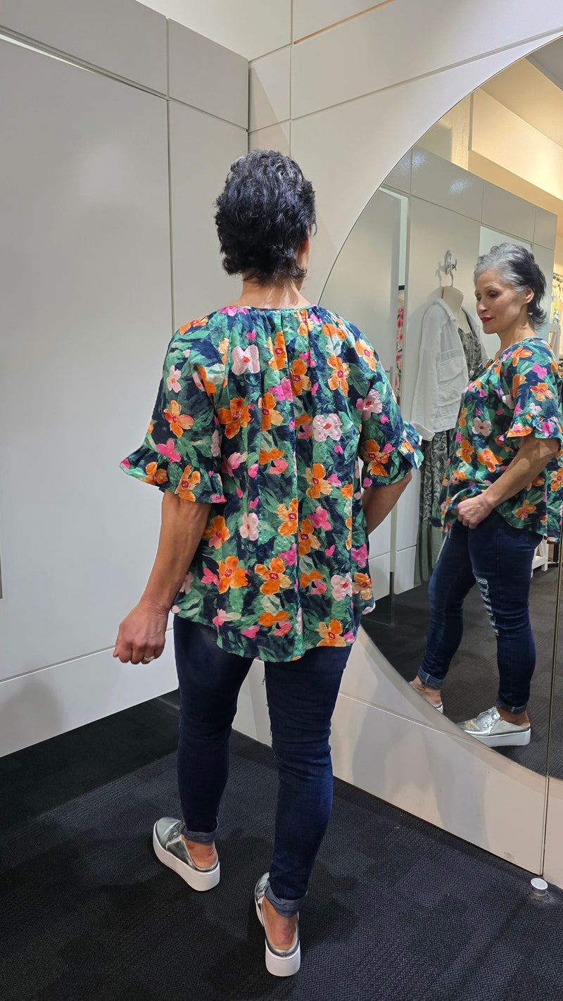 Person wearing a colorful floral shirt and dark jeans standing in a store. Tie Neck Top Navy