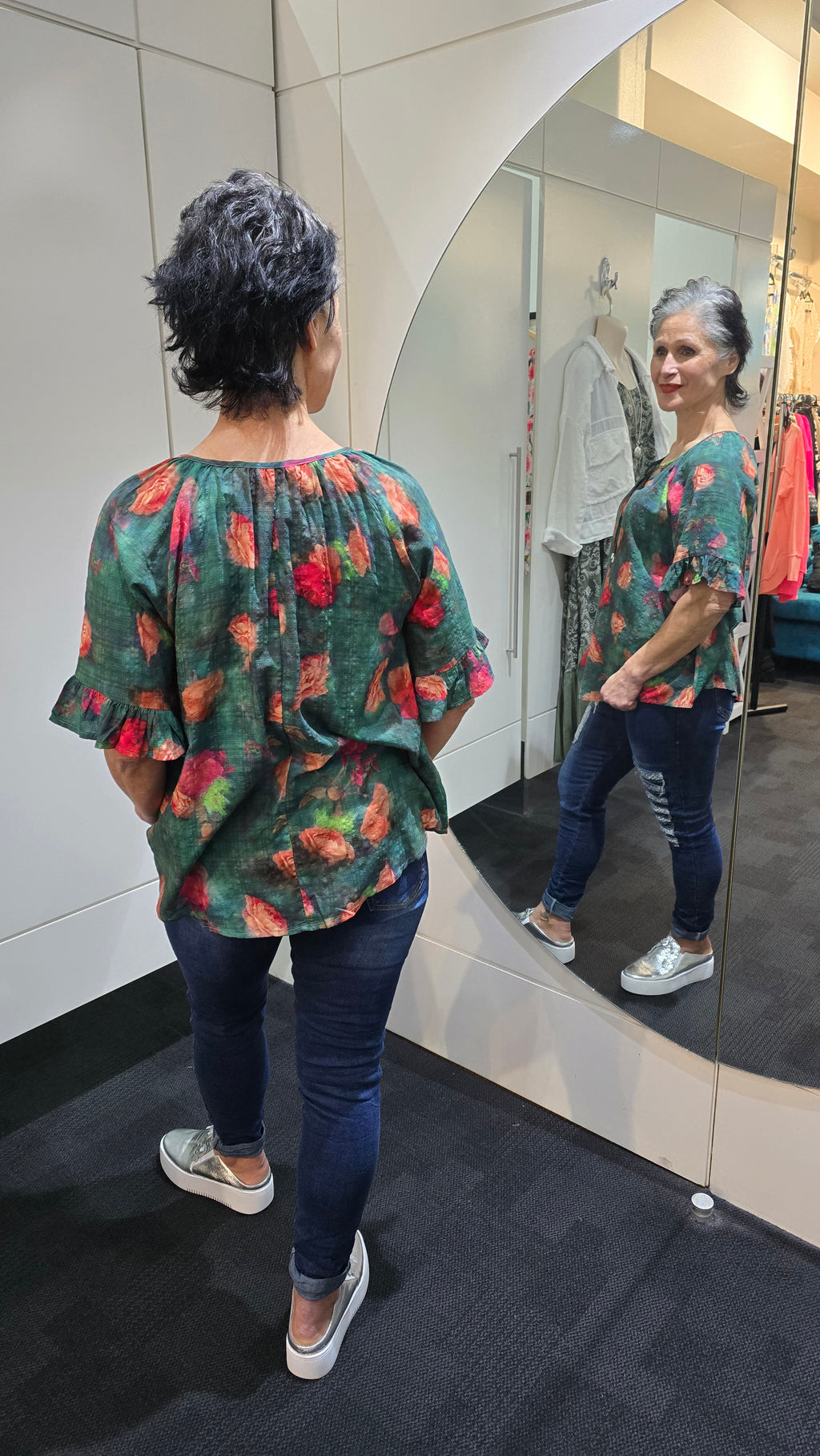 Person wearing a floral dress standing in front of a mirror. Tie Neck Top Green