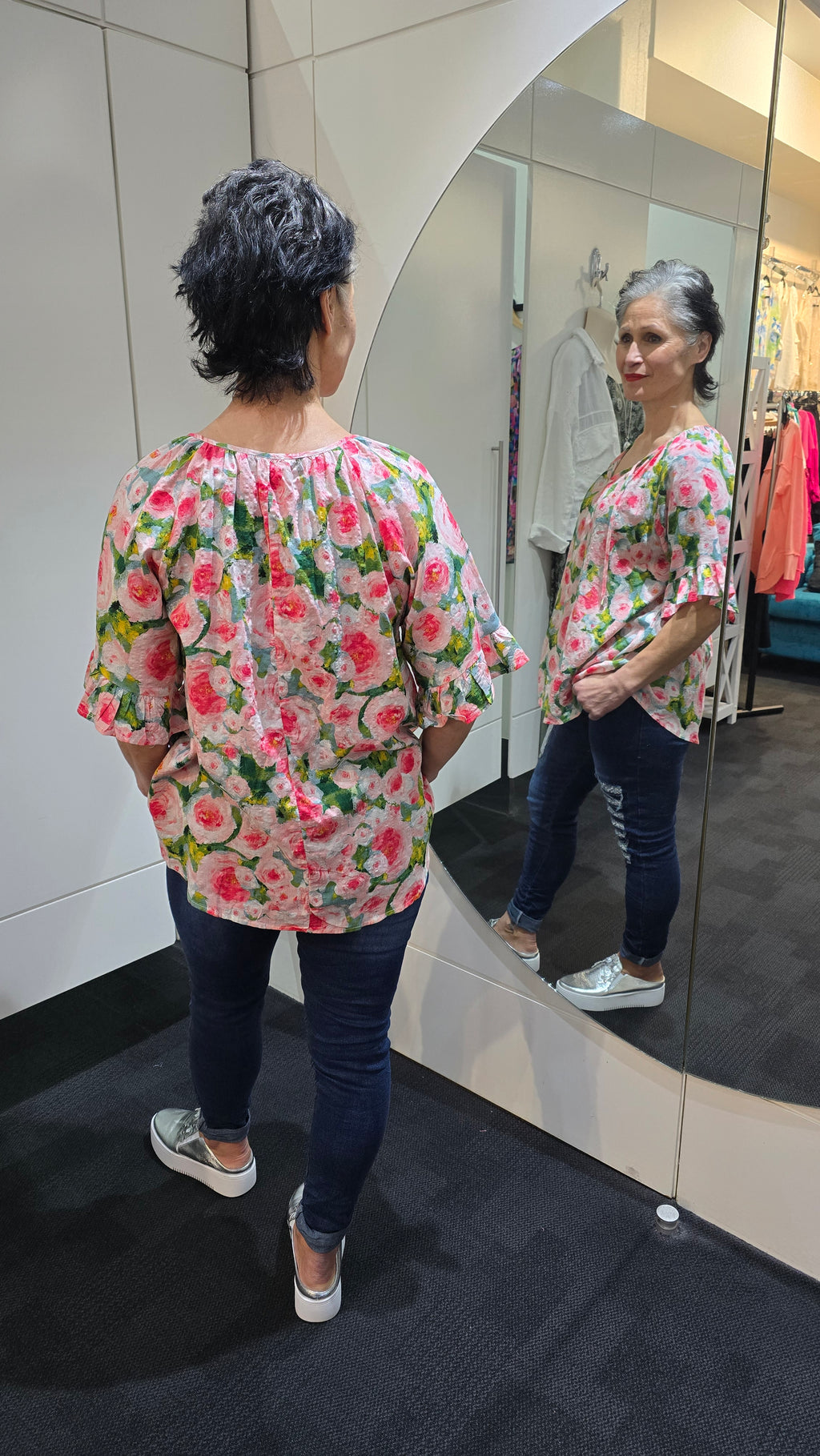 Person wearing a floral dress standing in front of a mirror. Tie Neck Top Pink