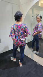 Person wearing a colorful floral blouse standing in front of a mirror. Tie Neck Top Multi