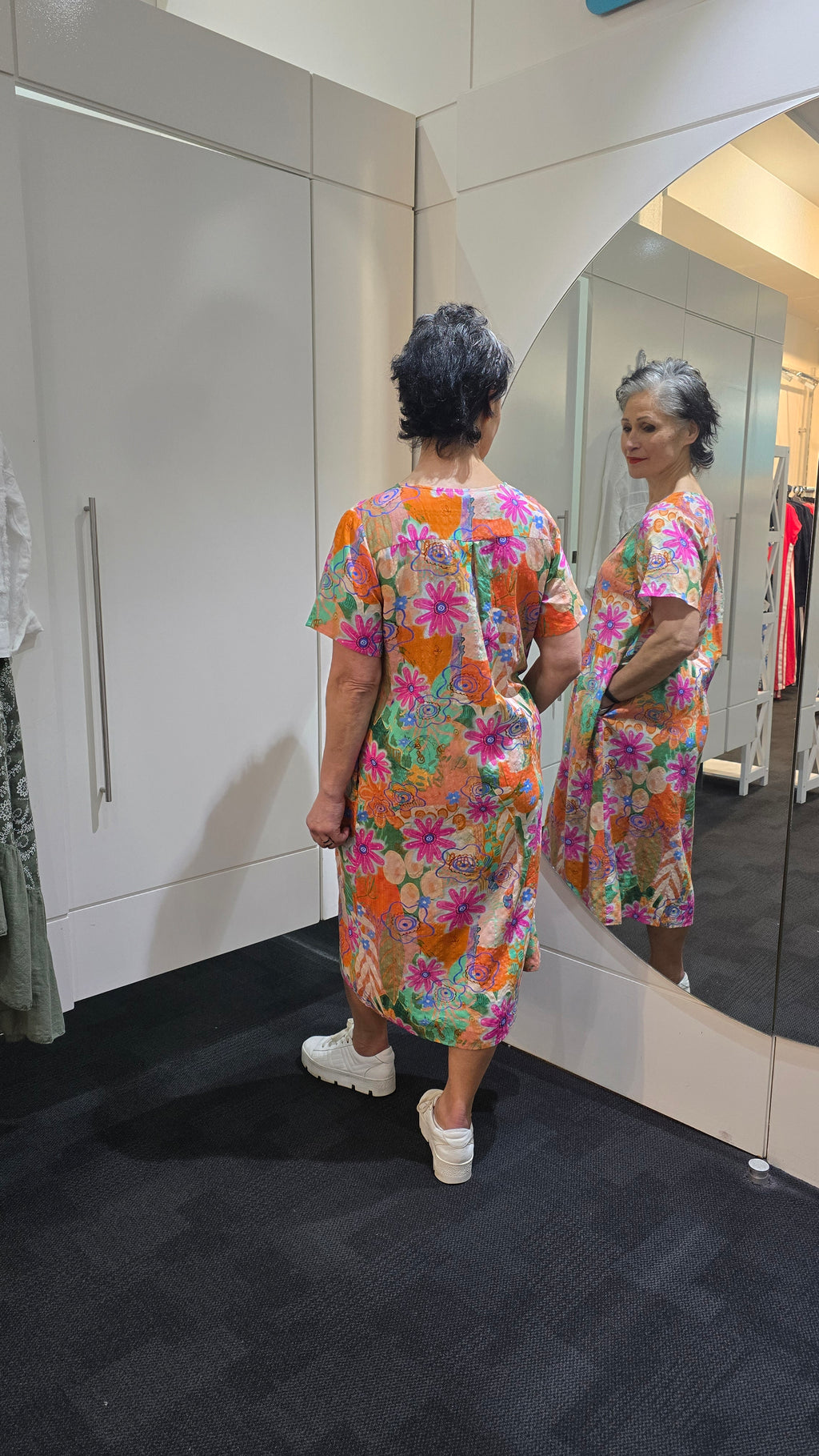 Person wearing a colorful floral dress standing in front of a mirror. Pleat Front Dress Orange