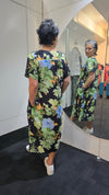 Person wearing a floral dress with a mirror reflection showing multiple people in similar attire. Pleat Front Dress Black