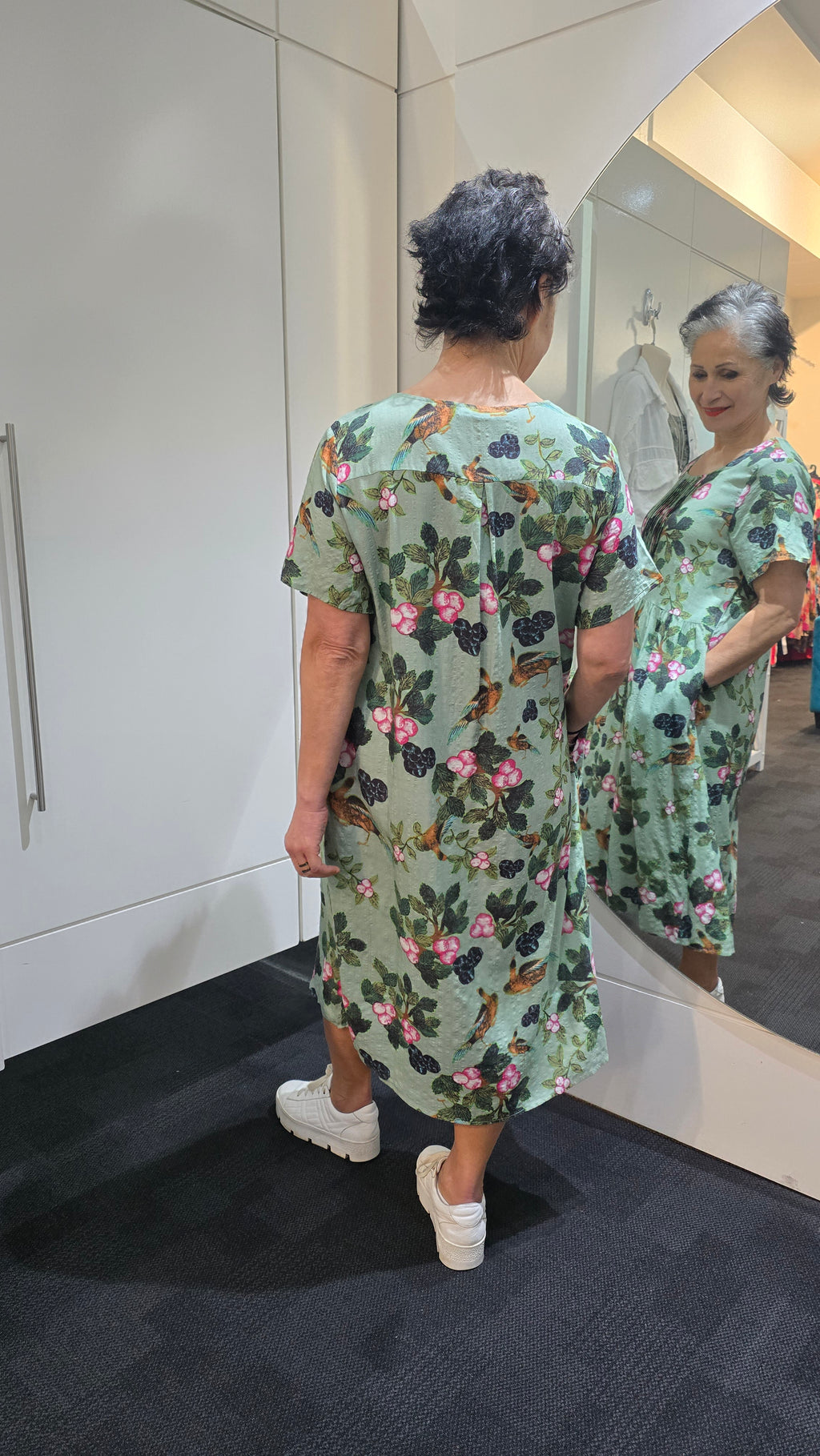 Woman wearing a floral dress standing in front of a mirror. Pleat Front Dress Green