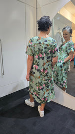 Woman wearing a floral dress standing in front of a mirror. Pleat Front Dress Green