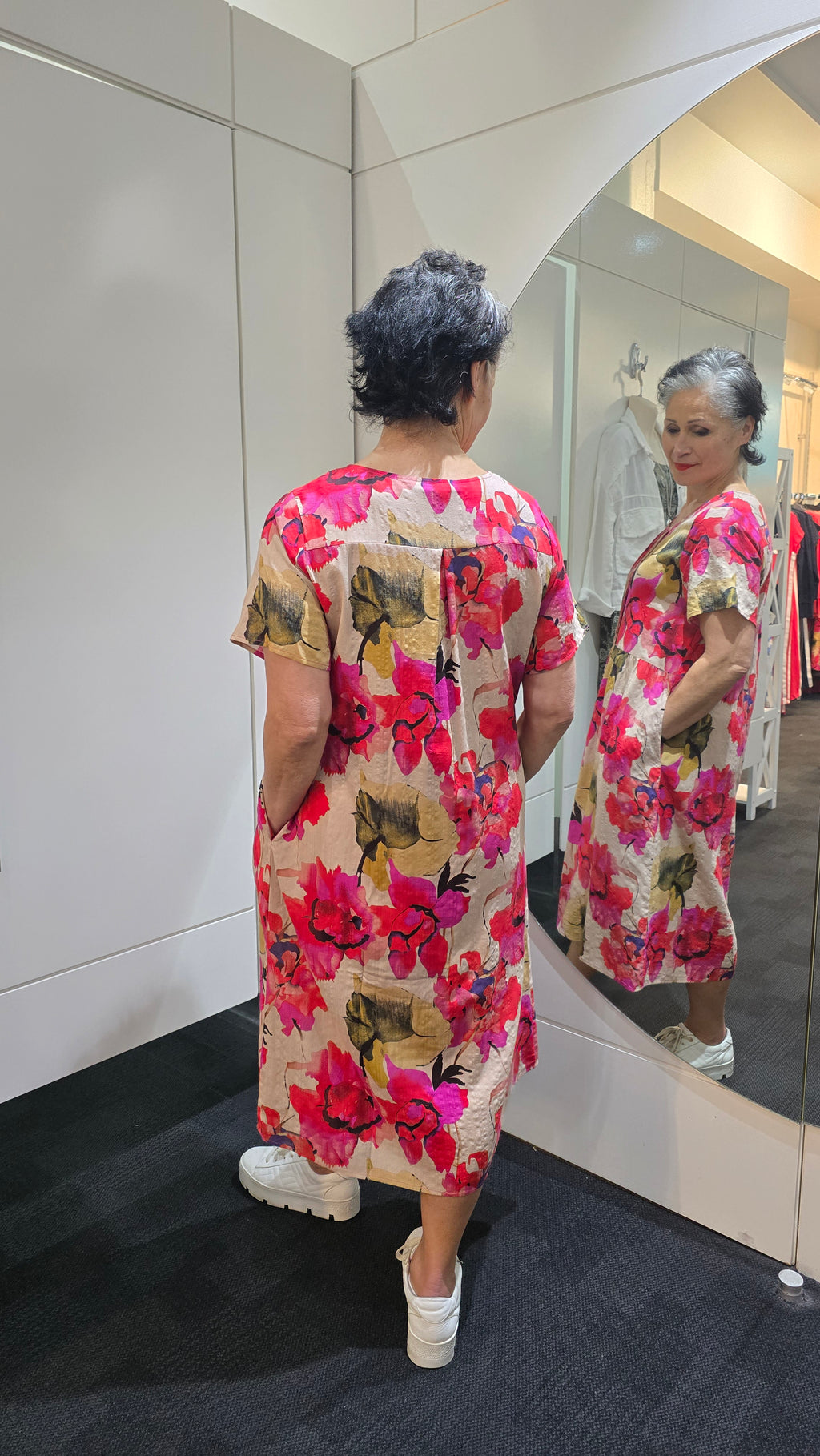 Woman wearing a floral dress standing in front of a mirror. Pleat Front Dress Red