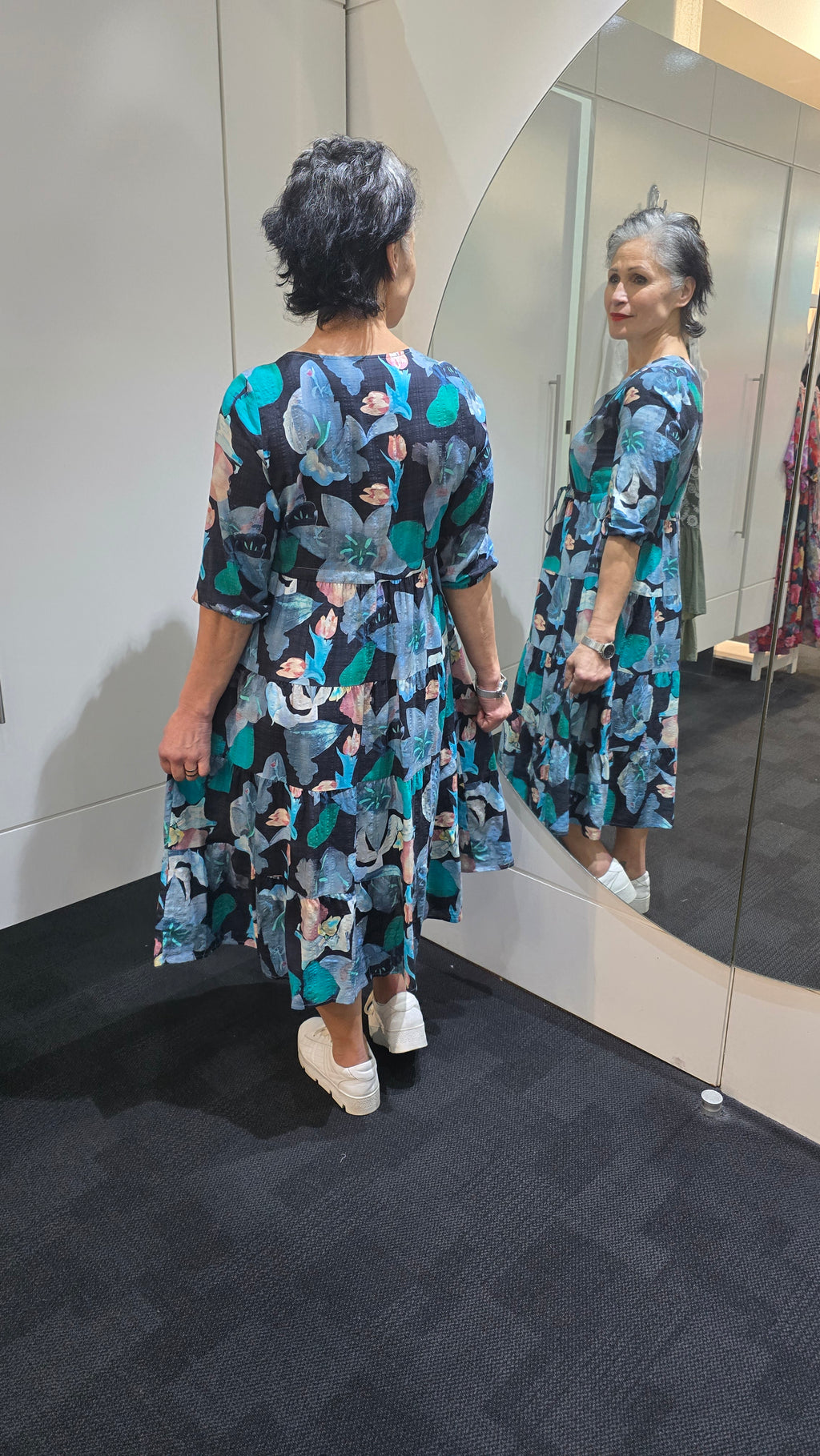 Person wearing a floral dress standing in front of a mirror. Tie Front Dress Blue