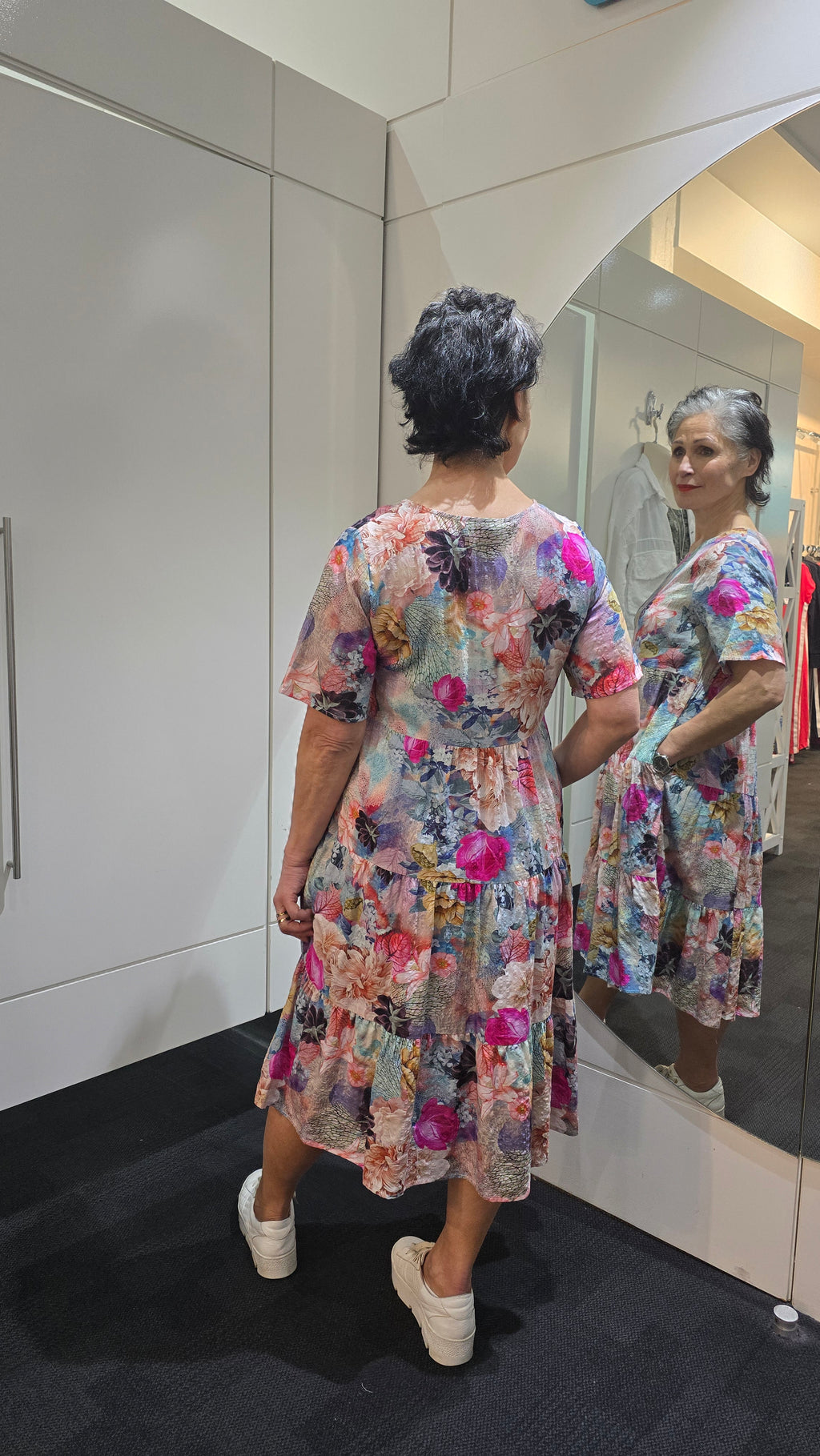 Woman wearing a colorful floral dress standing in front of a mirror. Tiered Dress Multi
