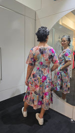 Woman wearing a colorful floral dress standing in front of a mirror. Tiered Dress Multi