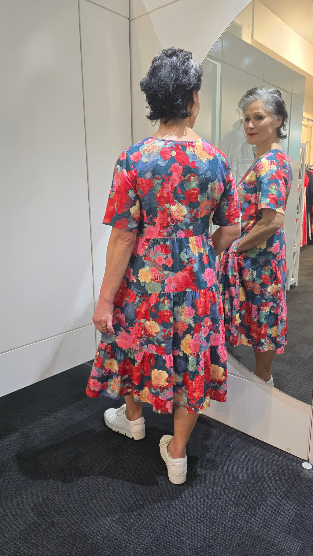 Person wearing a colorful floral dress standing in front of a mirror. Tiered Dress Red