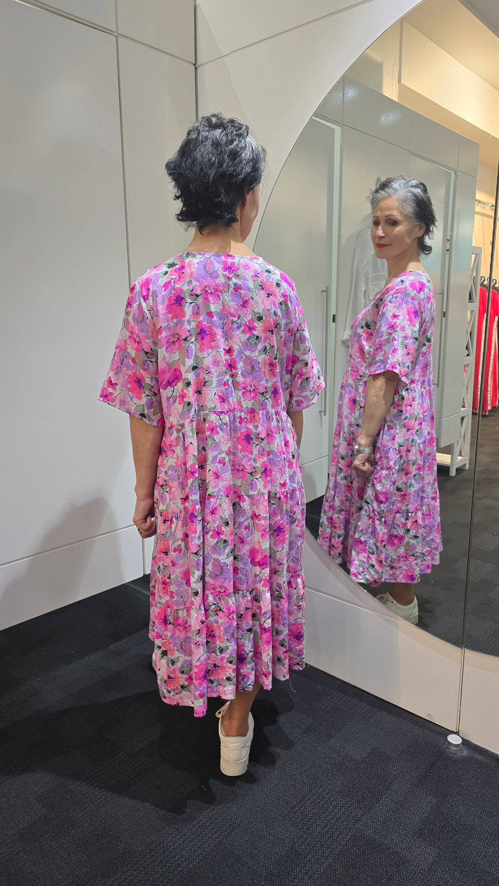Woman wearing a pink floral dress standing in front of a mirror. Tiered Dress Pink
