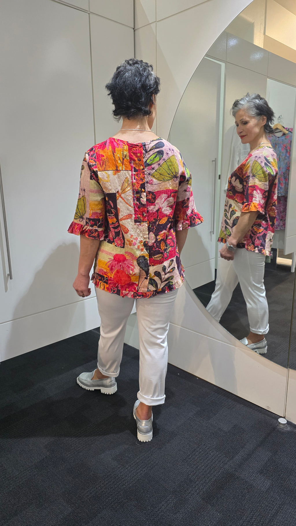 Person wearing a colorful floral jacket and white pants standing in front of a mirror. Round Neck Top Pink