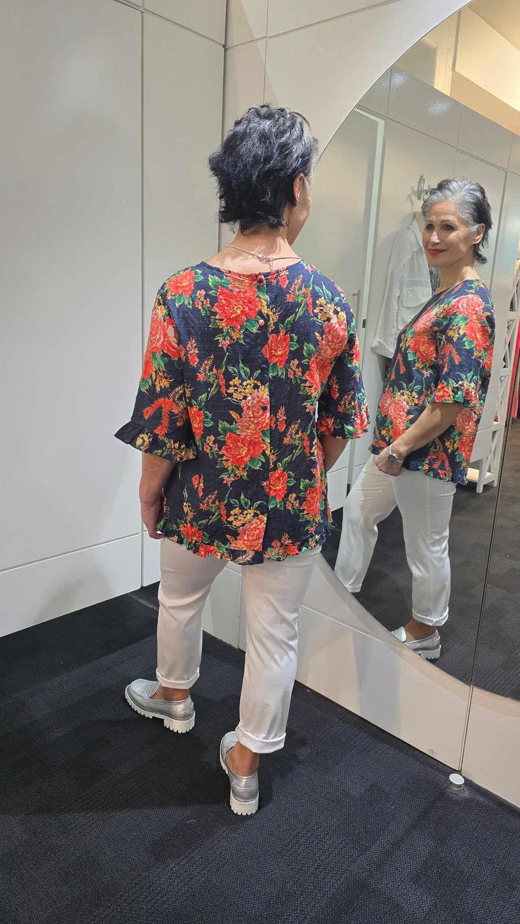 Person wearing a floral dress and white pants standing in front of a mirror. Round-Neck-Top-Multi