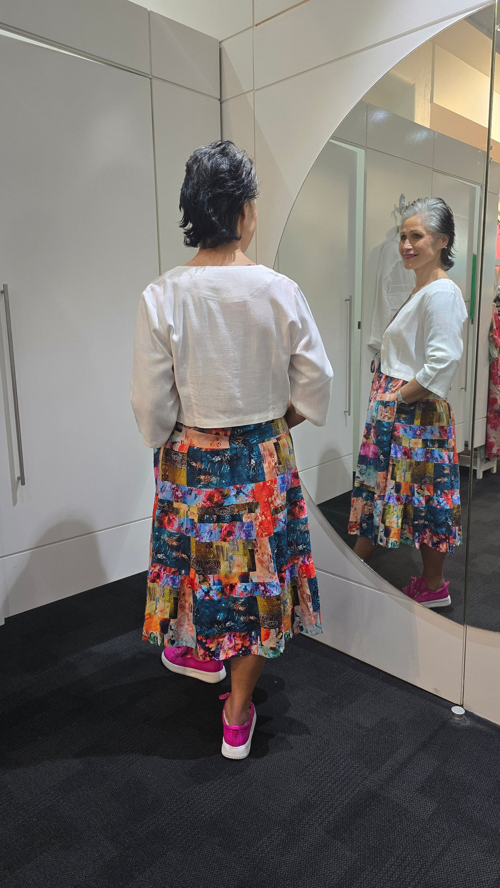 Person wearing a white shirt and colorful patterned pants standing in front of a mirror. Crop Jacket White
