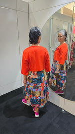 Person wearing an orange jacket and colorful patterned pants standing in front of a mirror. Crop Jacket Orange
