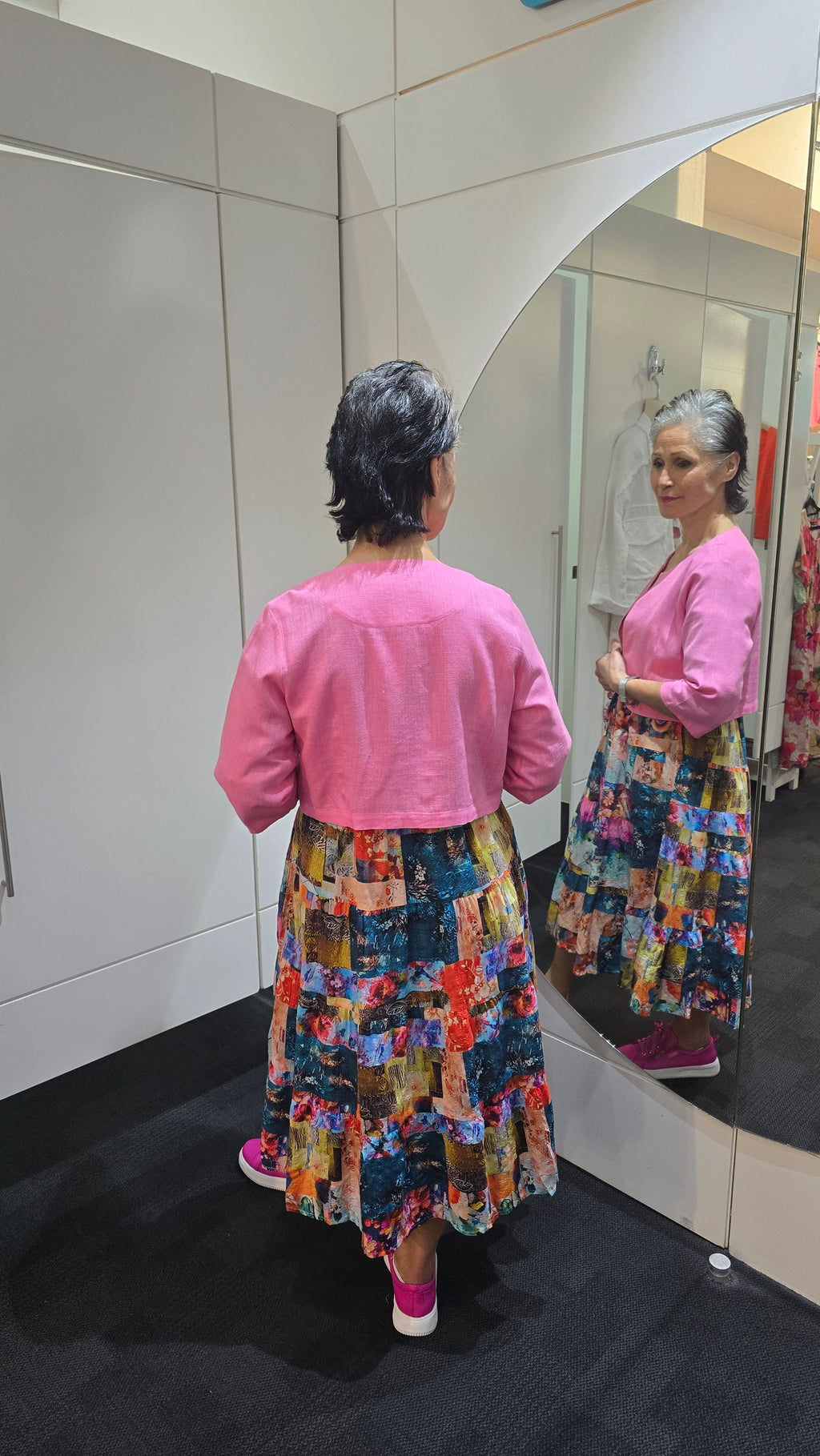 Person wearing a colorful dress and pink jacket standing in front of a mirror. Crop-Jacket-Pink