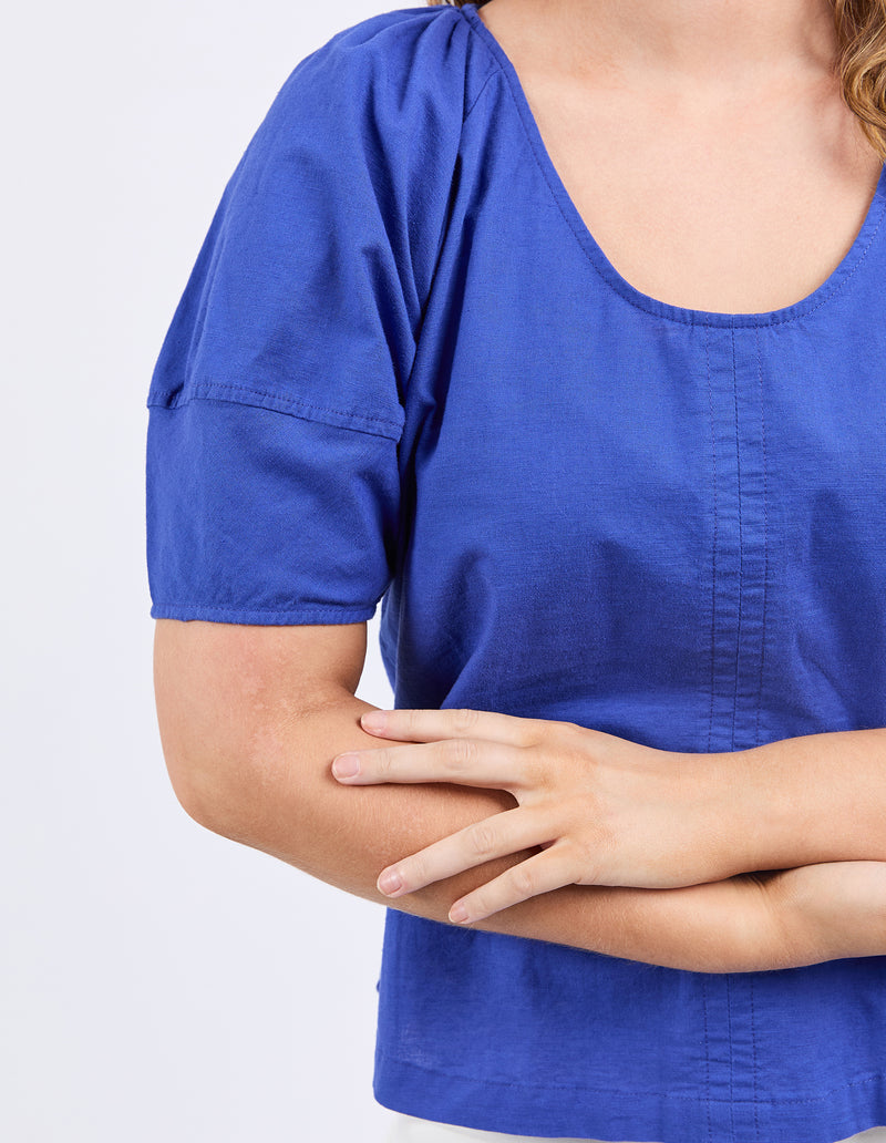 Person wearing a blue shirt with arms crossed on a light gray background
The Grove Top Ocean Blue