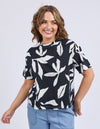 Woman wearing a black t-shirt with white leaf pattern and light blue jeans on a plain background
Mimosa Tee Black