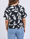 Person wearing a black t-shirt with white leaf pattern and light blue jeans on a plain background
Mimosa Tee Black