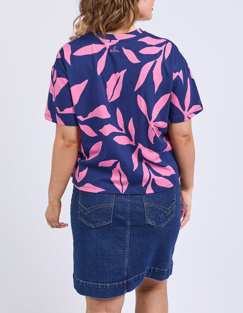 Person wearing a navy blue t-shirt with pink leaf pattern and denim skirt on a white background
Mimosa Tee Blue Depths