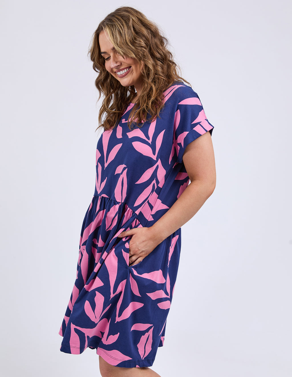 Woman wearing a navy dress with pink leaf pattern on a white background
Mimosa Dress Blue Depths