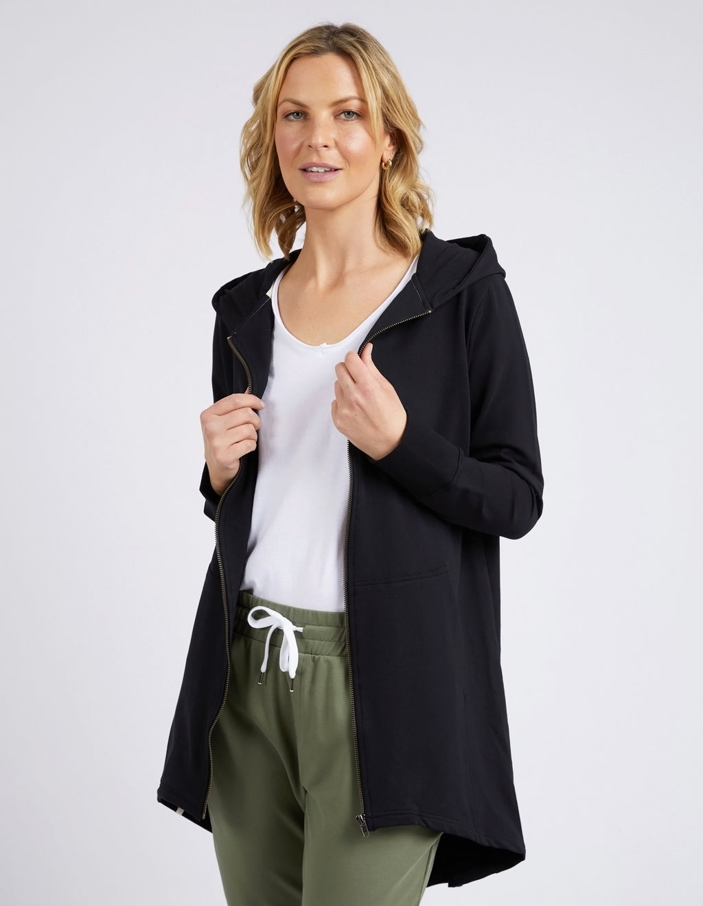Woman wearing a black coat over a white shirt and green pants on a light gray background
Mara Zip Hoodie Black