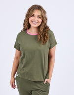 Woman wearing an olive green outfit with a pink collar on a white background
Cooper Tee Clover Green
