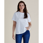 Woman wearing a white t-shirt with lace details and blue jeans on a beige background