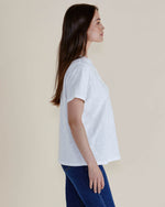 Woman wearing a white t-shirt and blue jeans against a plain background