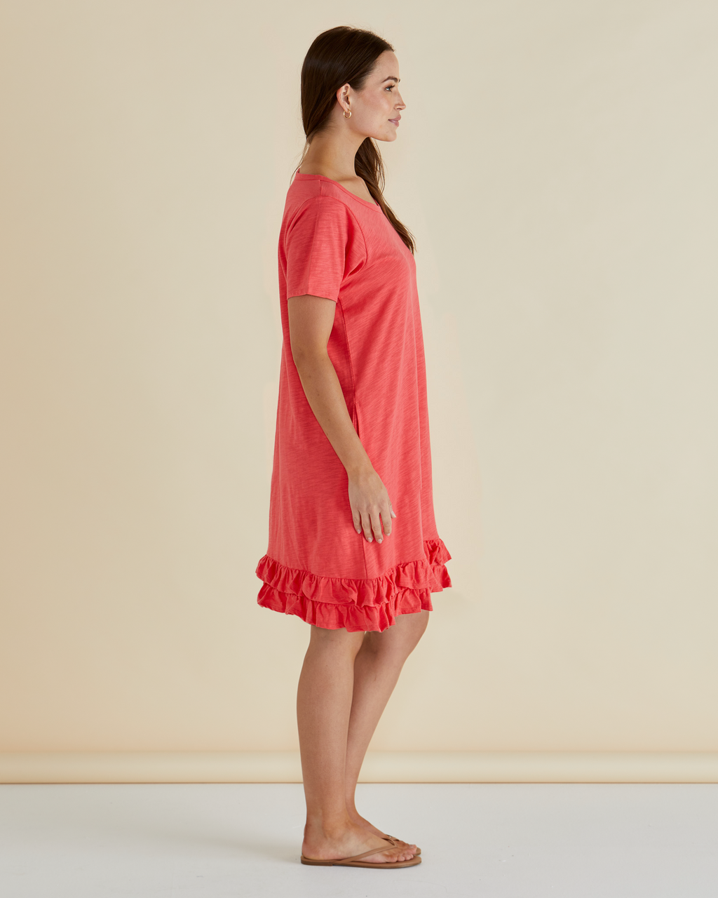 Woman wearing a coral dress with ruffle details on a beige background Aaliyah Dress Grapefruit