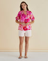 Woman wearing a colorful tie-dye top and white shorts on a beige Joanne Blouse Floral Pink background
