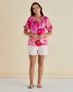 Woman wearing a colorful tie-dye top and white shorts on a beige Joanne Blouse Floral Pink background