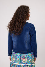 Woman wearing a blue denim jacket and colorful patterned skirt against a white background