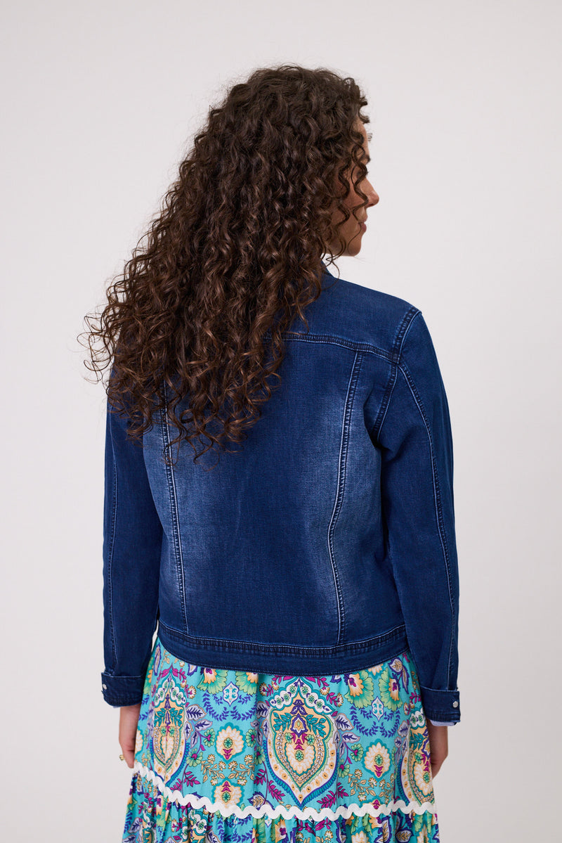 Woman wearing a blue denim jacket and colorful patterned skirt against a white background
