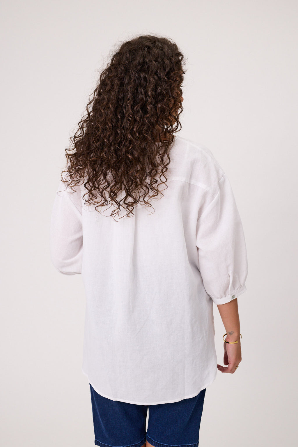 Person wearing a white shirt and blue pants with curly hair on a plain background Daisy Print Linen Top White