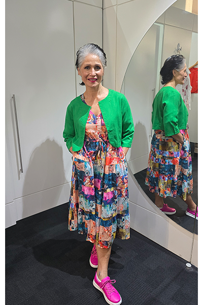 Woman in a colorful dress and green cardigan standing in front of a mirror. Crop Jacket Green