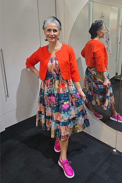 Woman in a colorful dress and orange cardigan standing in front of a mirror. Crop Jacket Orange