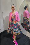 Woman wearing a colorful dress and pink cardigan standing in front of a mirror. Crop-Jacket-Pink