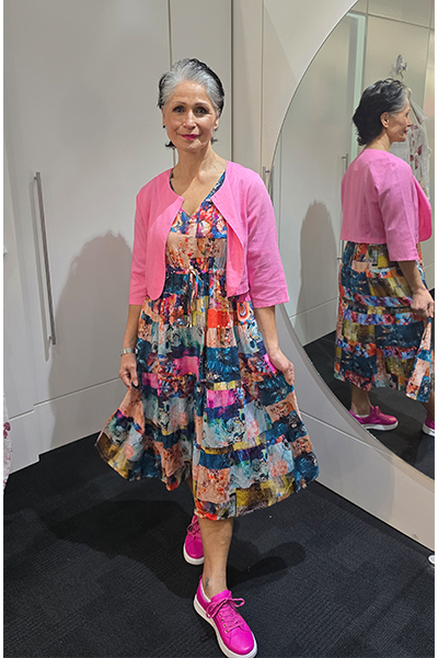 Woman wearing a colorful dress and pink cardigan standing in front of a mirror. Crop-Jacket-Pink