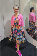 Woman wearing a colorful dress and pink cardigan standing in front of a mirror. Crop-Jacket-Pink