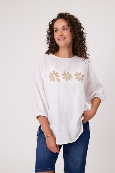 Woman wearing a white shirt with gold floral patterns and blue jeans on a white background Daisy Print Linen Top White