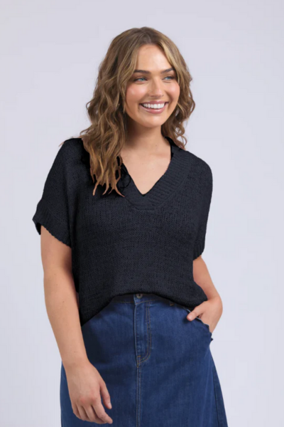 Woman wearing a black top and blue jeans against a light gray background Elba Knit Top Navy
